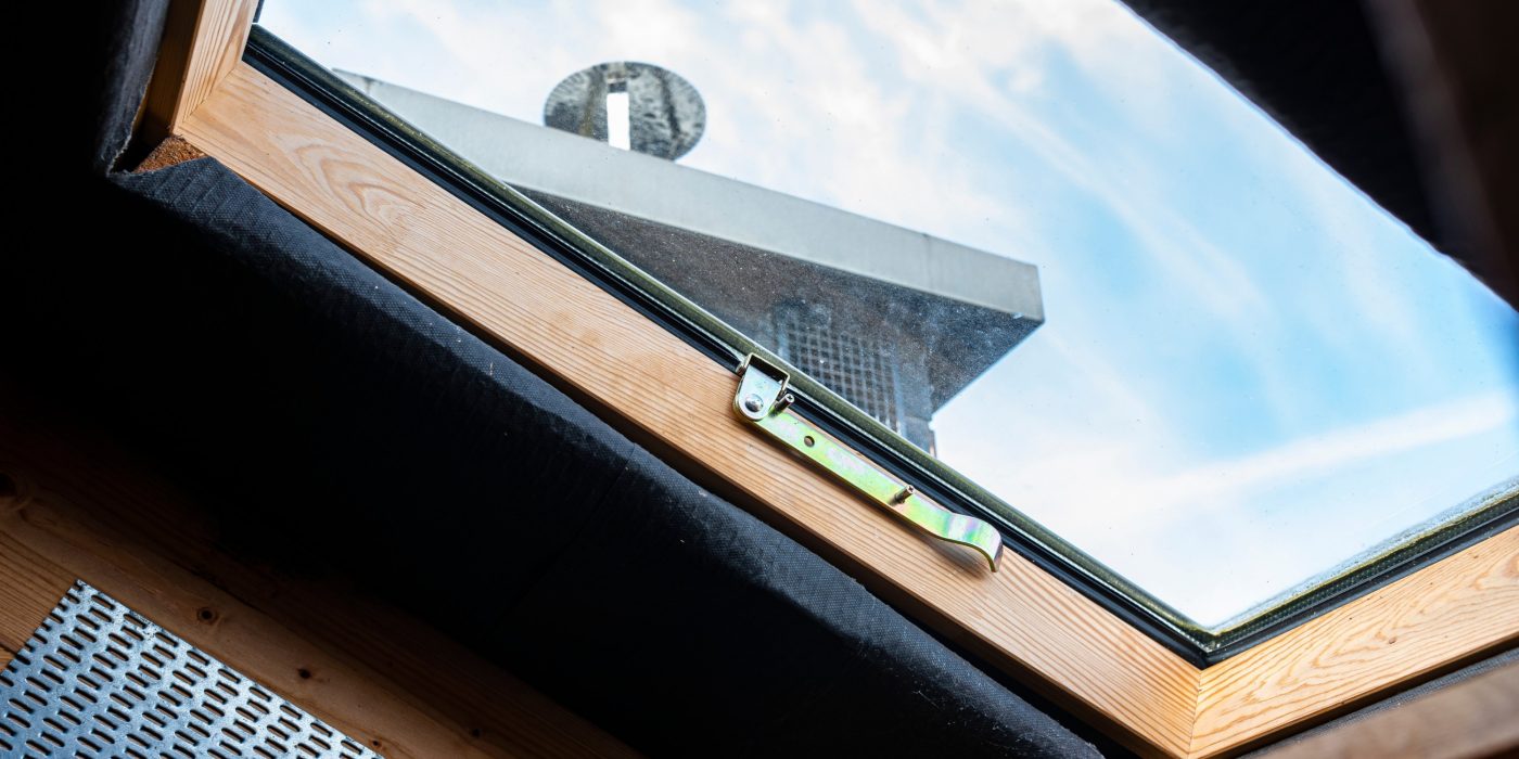 Roof hatch located in the attic for chimney sweep service, simple wooden frame with window, visible chimney.