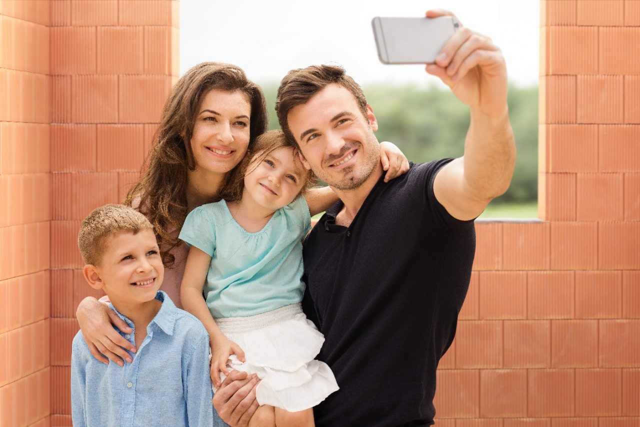 Parents with two kids taking a selfie with mobile phone inside new built house in front of bare clay block walls