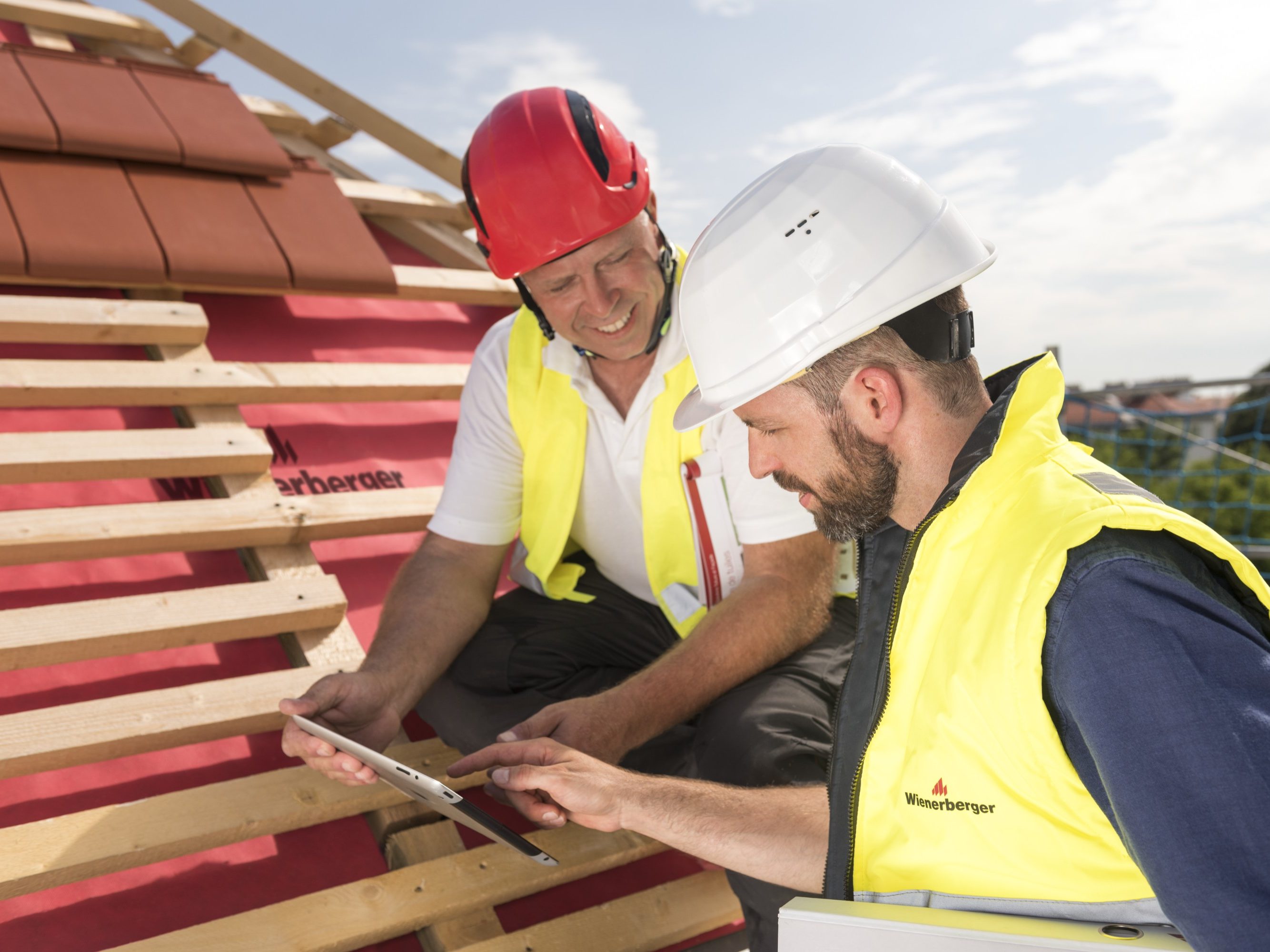 Urban roofer and product manager with tablet computer explaining product advantages to urban roofers wearing safety jackets and hard hats