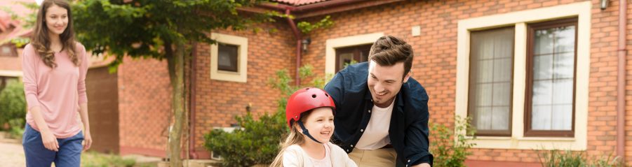 Father protecting little girl while learning to ride the bike while mother watches them