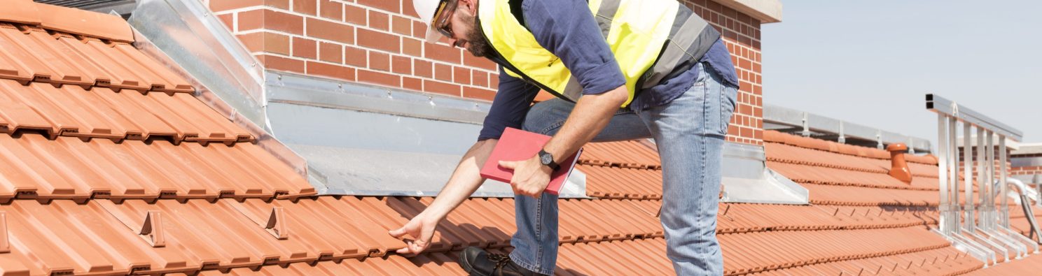 Product manager checking ventilation roof tiles in front of chimney standing on the roof wearing hard hat and safety jacket