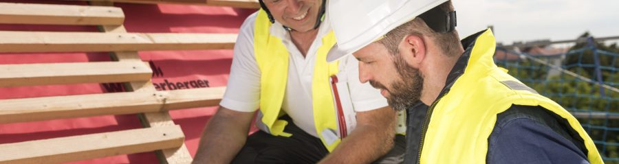 Urban roofer and product manager with tablet computer explaining product advantages to urban roofers wearing safety jackets and hard hats