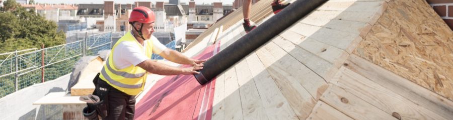 Urban roofers applying roof underlay sheet wearing hard hat and safety jacket brick chimney