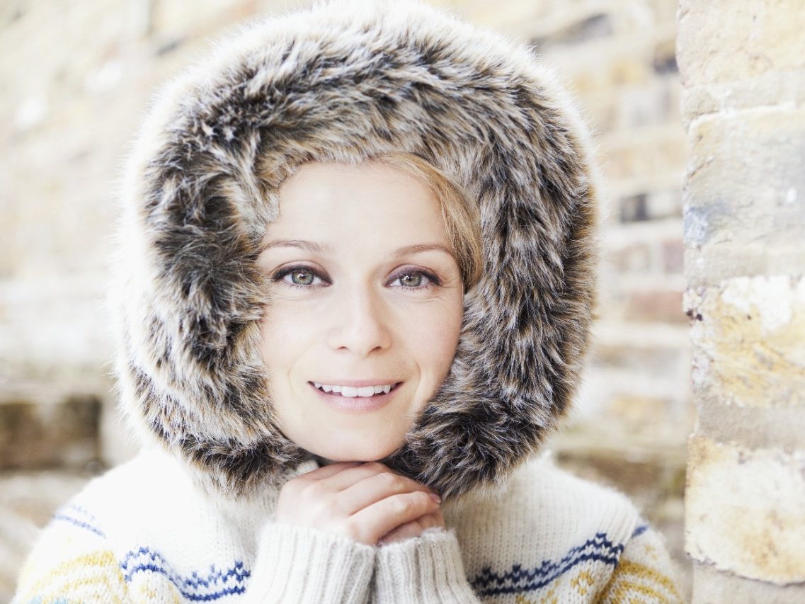 Woman with fur-collar surrounded by brick-lined wall