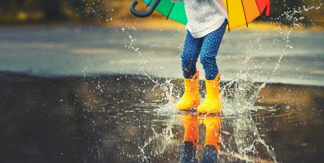 Feet of child in yellow rubber boots jumping over a puddle in the rain