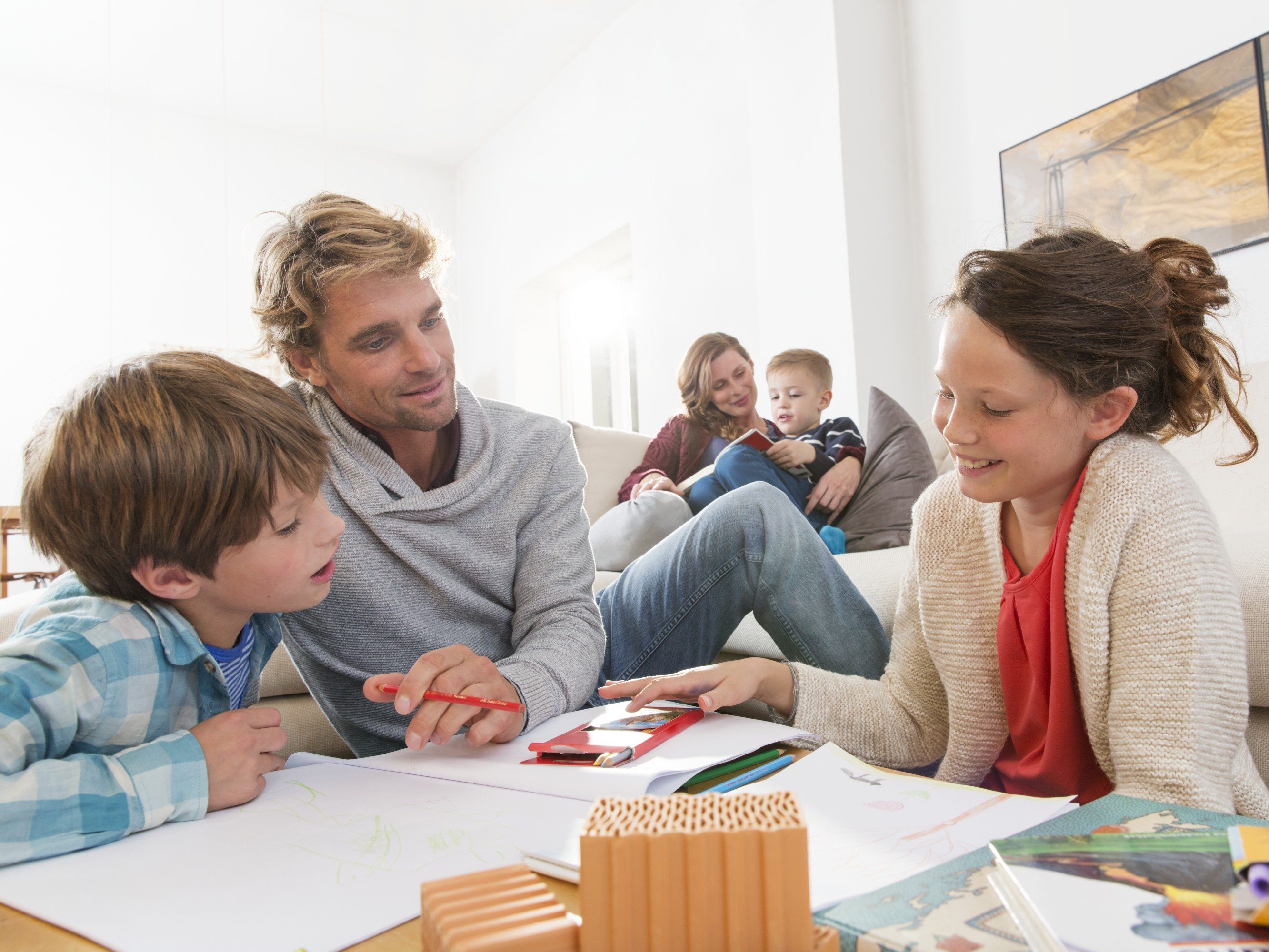 Father with two kids sketching and mother with boy reading a book in living room