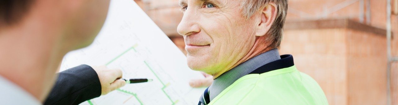 Men with safety jackets and construction plan in front of new built house