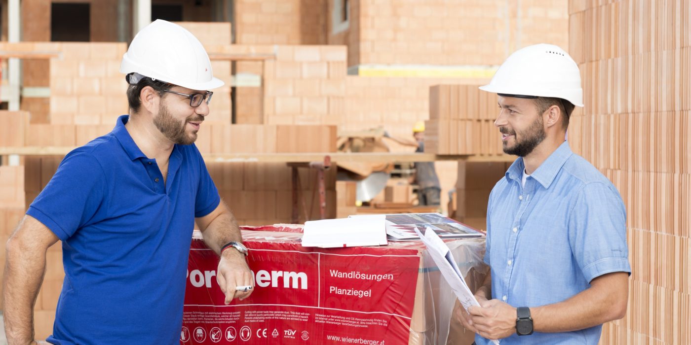 Building professionals talking at construction site next to foil wrapped pallette of brick blocks. > There is another version of this image available with another worker in the background