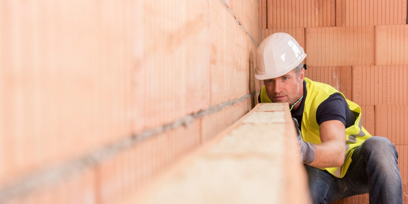 Construction worker checking alignment of mineral-wool filled clay block