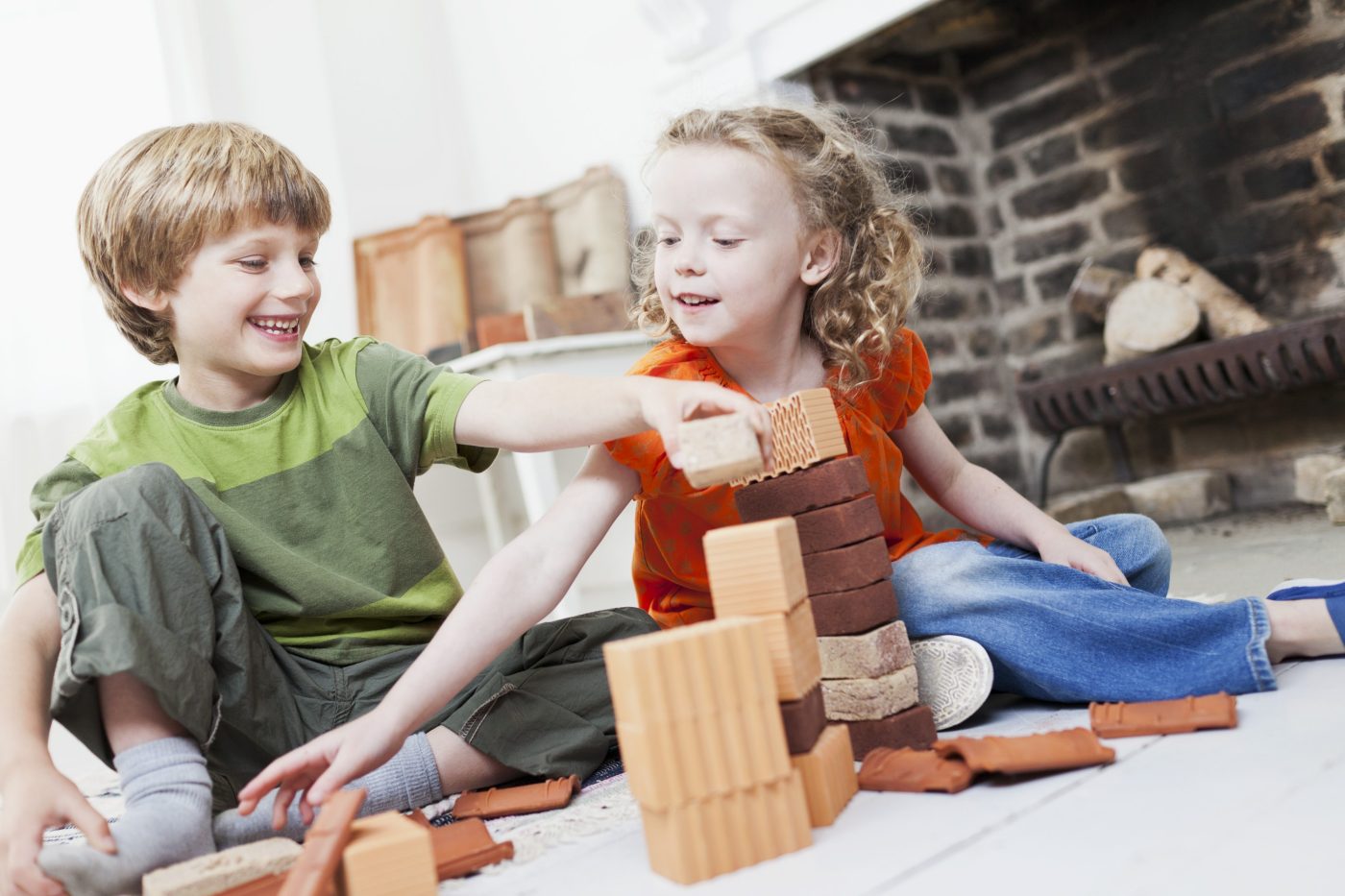Boy and girl playing with miniature bricks, clay blocks and clay roof tiles in front of fireplace