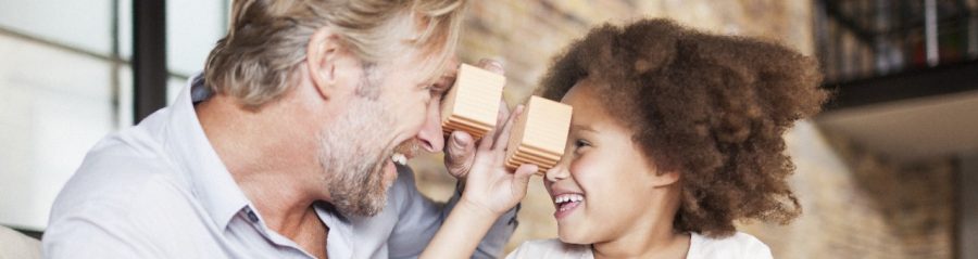 Man and girl sitting on sofa holding miniature clay blocks in front of brick-built façade
