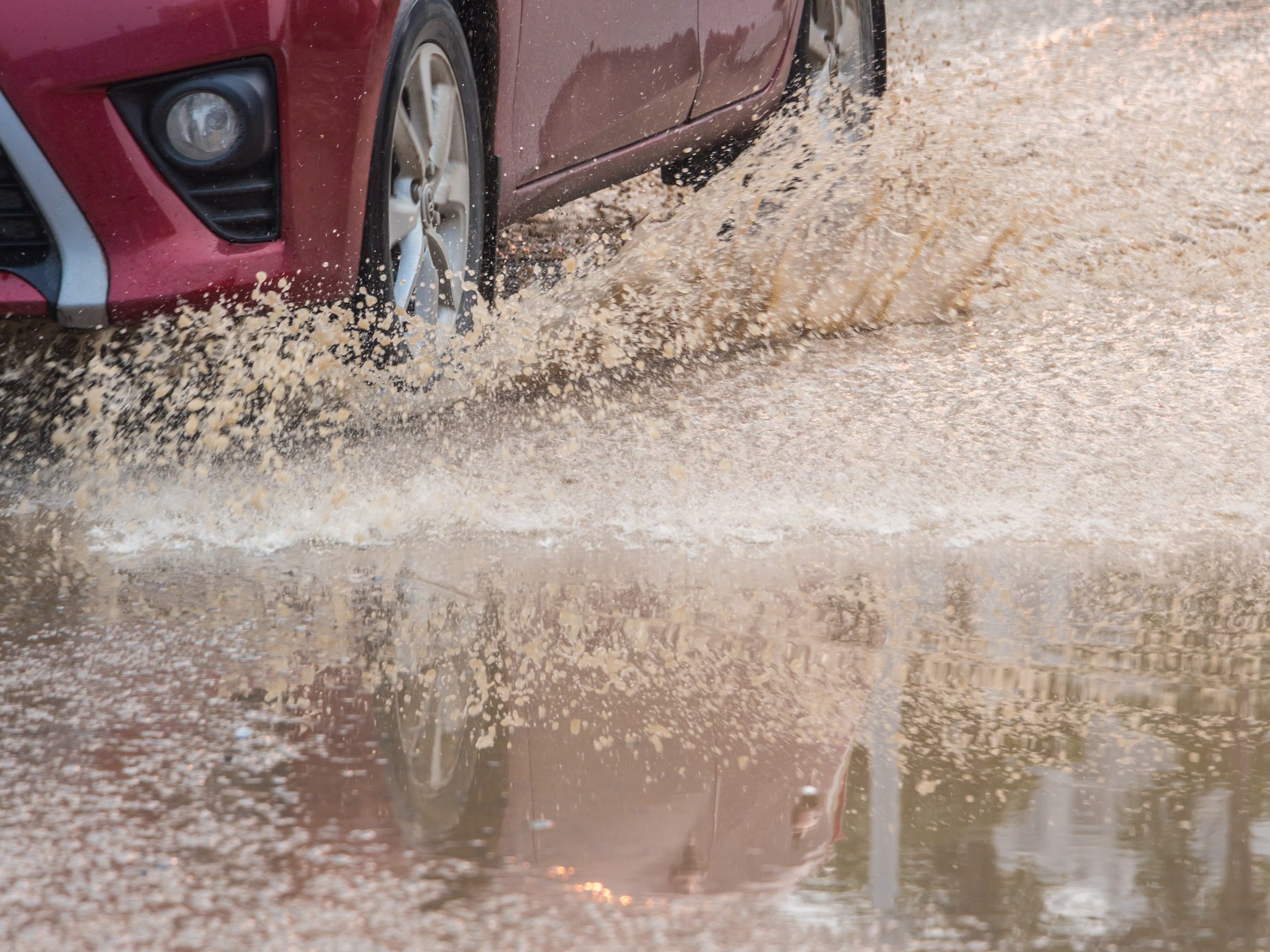 A red car speeding through the sewage road splashing yellow water splash