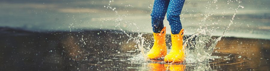 Feet of child in yellow rubber boots jumping over a puddle in the rain